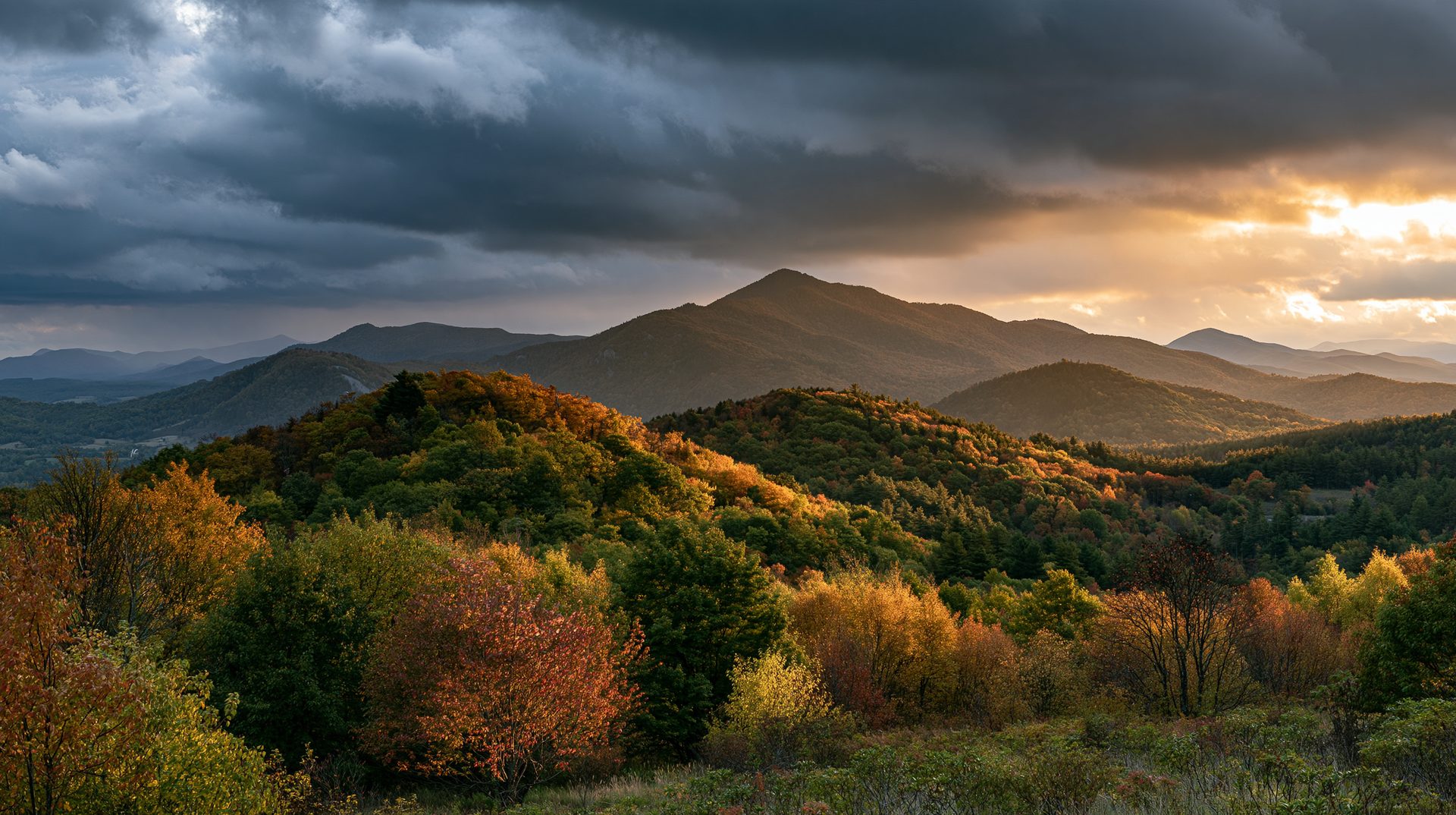 A wide scenic view of West Virginia mountain ridges covered in colorful autumn trees, split between dark storm clouds on the left and a brilliant golden sunset breaking through on the right.