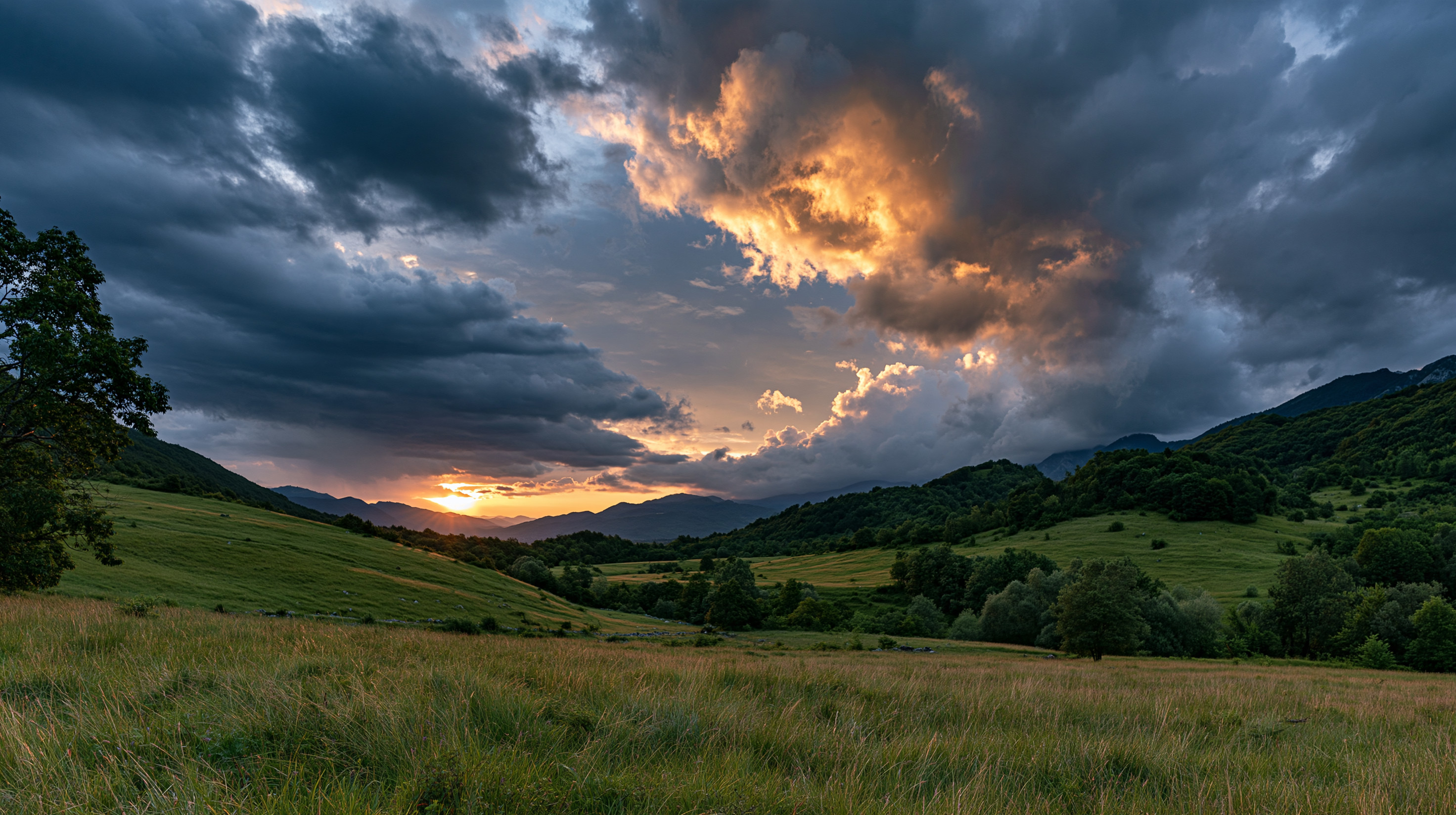 A spectacular wide-angle landscape photograph of a green mountain valley in Bosnia at sunset, featuring a dramatic stormy sky illuminated by golden and fiery orange light.