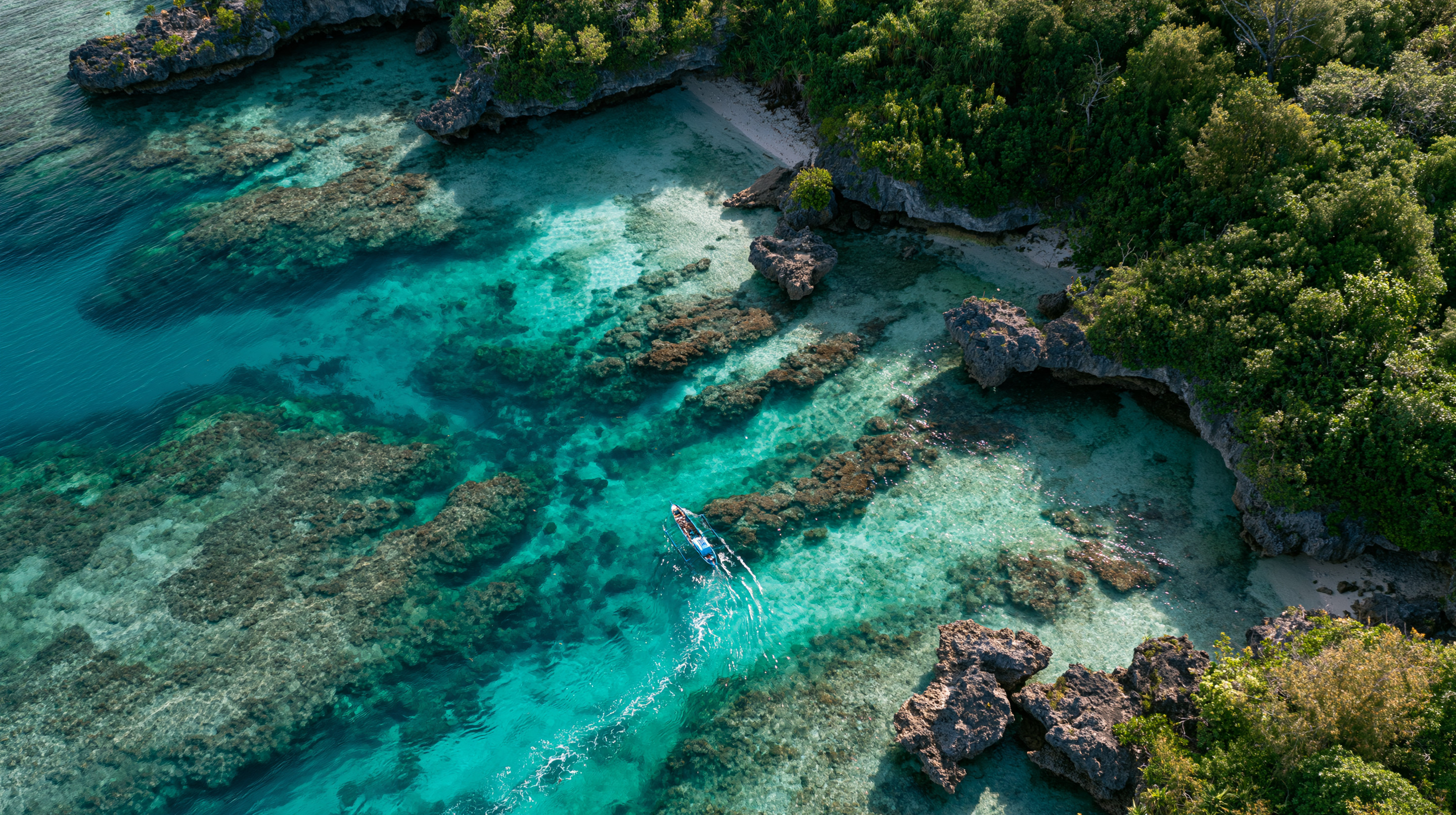 High-angle aerial view of a traditional small outrigger boat navigating a narrow, clear turquoise water channel through a shallow coral reef next to a rocky, forested coastline in Vanuatu.
